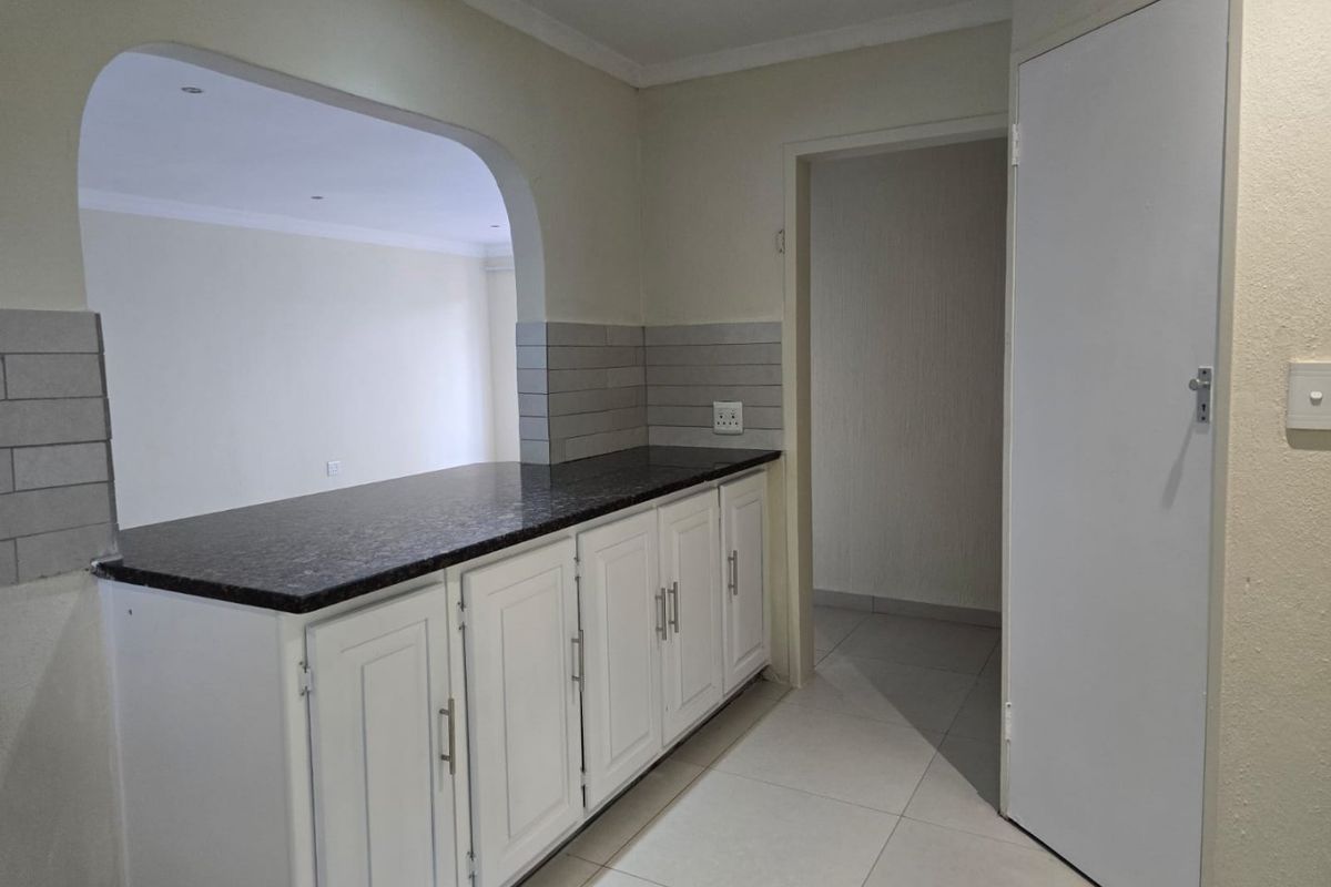A clean, empty kitchen area featuring white cabinetry, dark granite countertops, a tiled backsplash, and an open-plan archway leading to the living space.