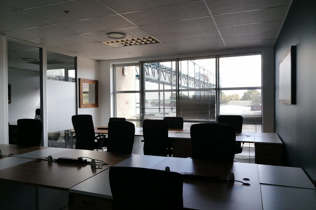 A professional commercial office space featuring large windows, suspended ceilings, and integrated desk workstations with glass partition walls.