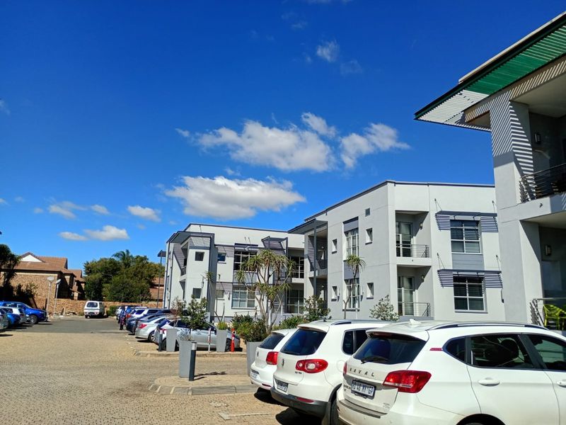 Exterior view of a modern multi-story commercial office building with a paved parking lot and clear blue sky.