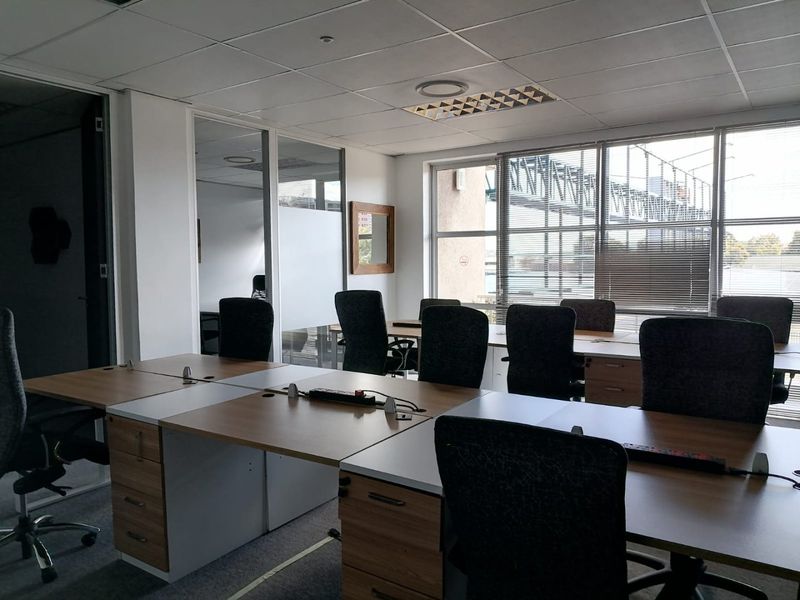 A functional commercial office space featuring large windows, glass partitions, suspended ceilings, and integrated desk workstations.