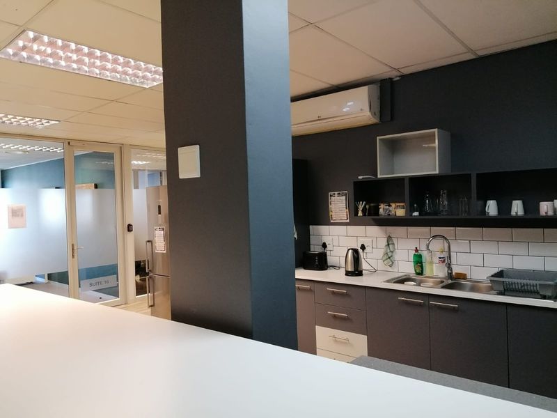 A functional office kitchenette featuring dark cabinetry, a subway tile backsplash, stainless steel sink, and integrated air conditioning unit.