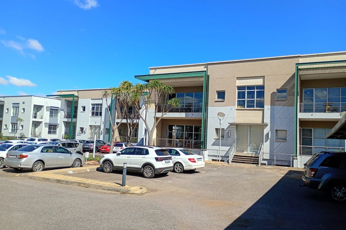 Front exterior view of a multi-story commercial office complex featuring paved parking, modern facade finishes, and balcony access.