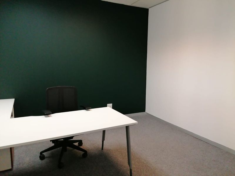 A clean, minimalist office space featuring a dark accent wall, neutral white walls, and grey carpet flooring, suitable for a professional workspace.