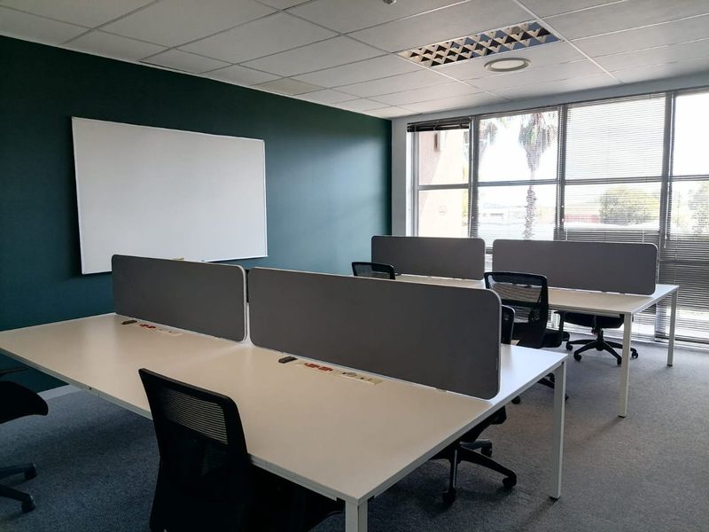A professional office space featuring a suspended ceiling, recessed lighting, large windows with blinds, and a wall-mounted whiteboard.