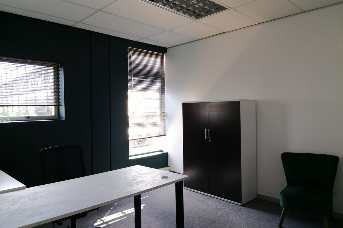 A functional commercial office space featuring carpeted flooring, suspended ceiling with recessed lighting, and large windows with fitted venetian blinds.