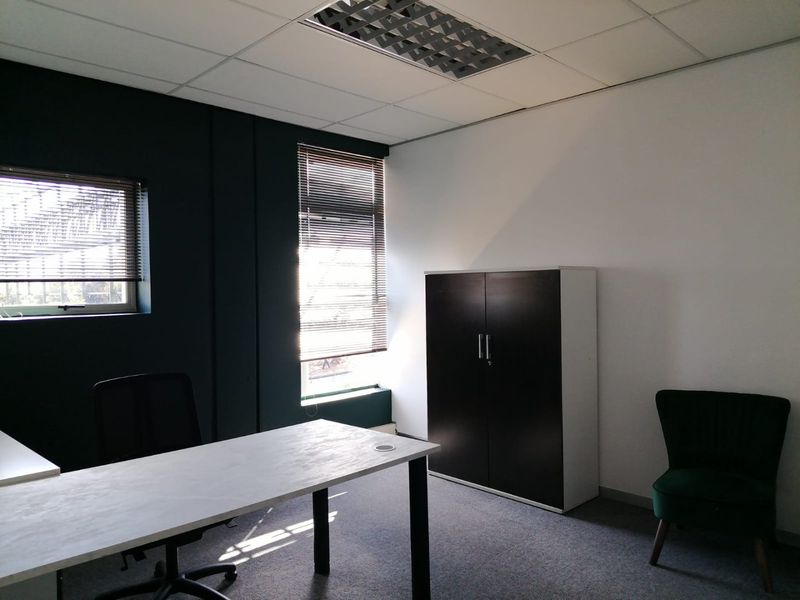 A functional commercial office space featuring carpeted flooring, suspended ceiling with recessed lighting, and large windows with fitted venetian blinds.