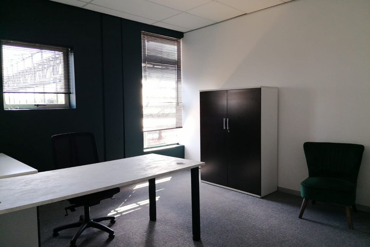 A functional office space featuring carpeted flooring, a suspended ceiling, and large windows with fitted venetian blinds for natural light control.