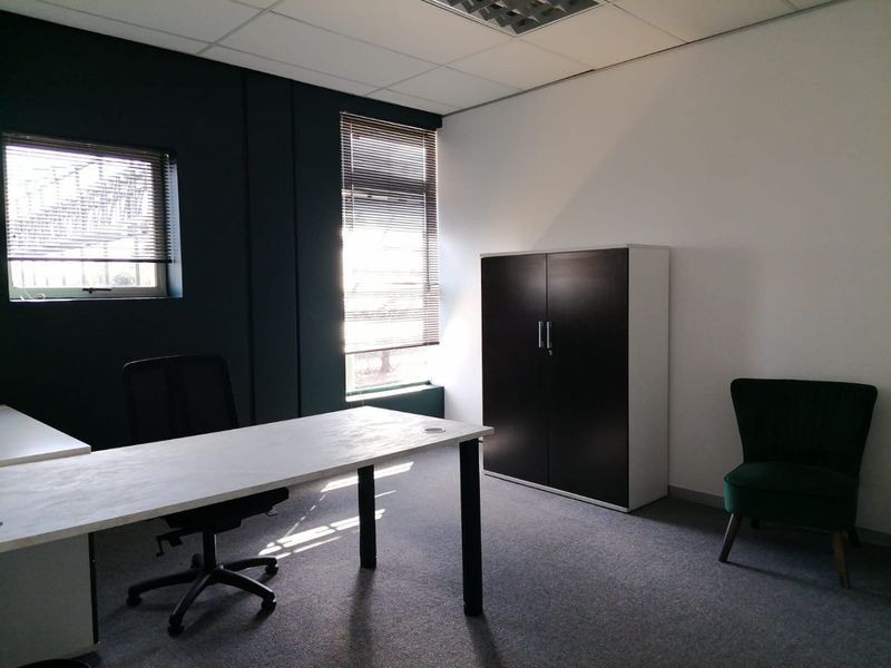 A functional office space featuring carpeted flooring, a suspended ceiling, and large windows with fitted venetian blinds for natural light control.
