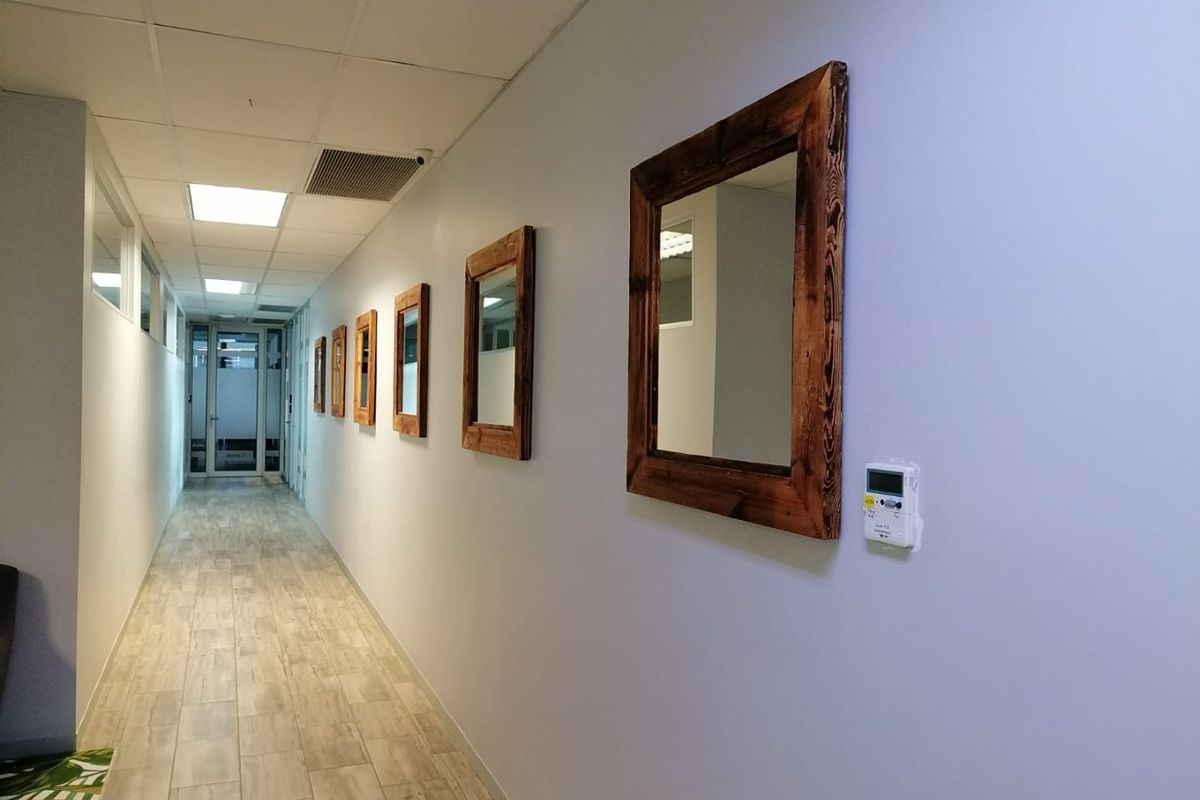 A clean, well-lit commercial hallway featuring wood-look tile flooring, a suspended ceiling with recessed lighting, and a wall-mounted digital thermostat.