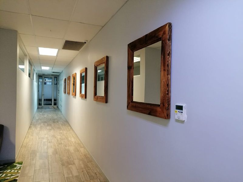 A clean, well-lit commercial hallway featuring wood-look tile flooring, a suspended ceiling with recessed lighting, and a wall-mounted digital thermostat.