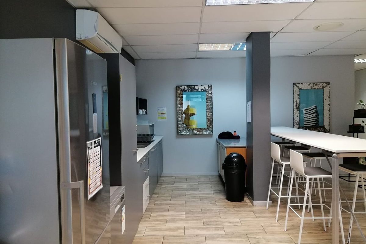 A functional commercial kitchen area featuring built-in cabinetry, durable tiled flooring, and a split-system air conditioning unit, suitable for office or staff breakroom use.