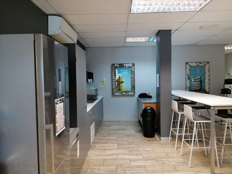 A functional commercial kitchen area featuring built-in cabinetry, durable tiled flooring, and a split-system air conditioning unit, suitable for office or staff breakroom use.