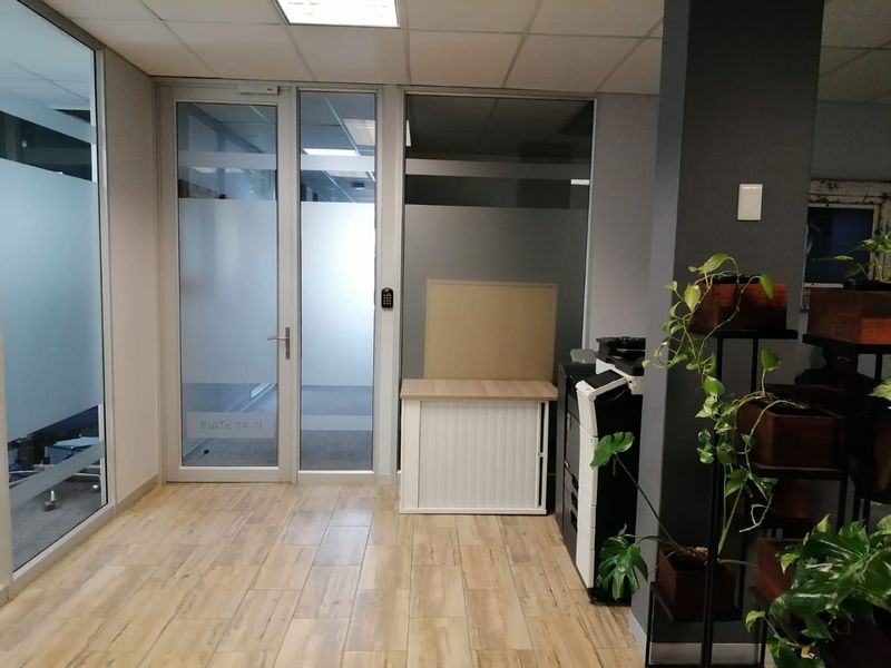 A modern commercial office entrance featuring glass partitioning, wood-look tile flooring, and secure keypad access control.