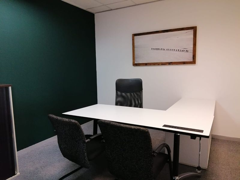 A professional office space featuring a modern desk setup, carpeted flooring, and a dark green accent wall.