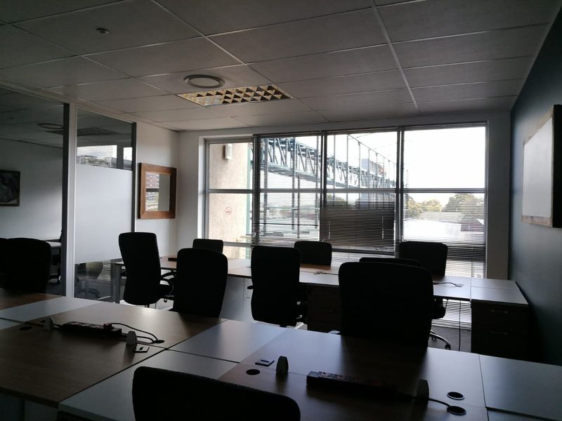 A functional commercial office space featuring built-in desk workstations, suspended ceilings with recessed lighting, and large windows providing natural light and exterior views.