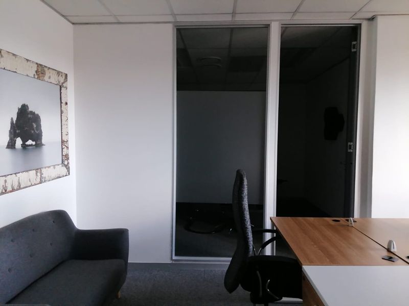 A functional office space featuring a glass partition wall, suspended ceiling, and carpeted flooring, suitable for a professional work environment.