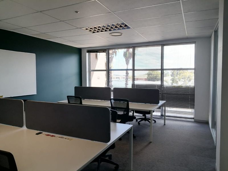 A bright, professional office space featuring a suspended ceiling, large windows with venetian blinds, and carpeted flooring, suitable for a collaborative work environment.