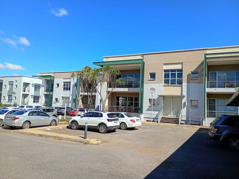 Front exterior view of a multi-story commercial office complex featuring paved parking, modern facade finishes, and balcony access.