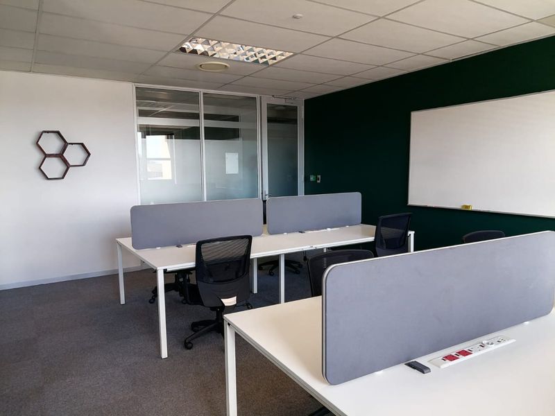 A modern commercial office space featuring a glass partition, suspended ceiling, whiteboard, and integrated desk power points.