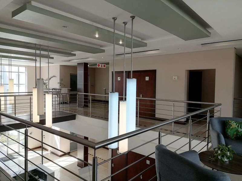 Spacious commercial mezzanine hallway featuring modern pendant lighting, stainless steel balustrades, and a contemporary drop-ceiling design with recessed panels.