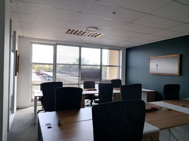 A professional office space featuring a suspended ceiling, recessed lighting, large windows with blinds, and a modern dark accent wall.