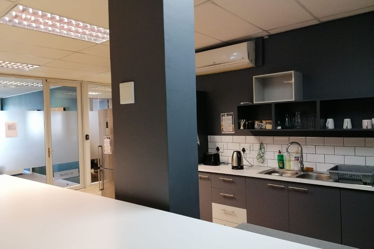 A functional office kitchenette featuring dark cabinetry, a subway tile backsplash, stainless steel sink, and integrated air conditioning unit.