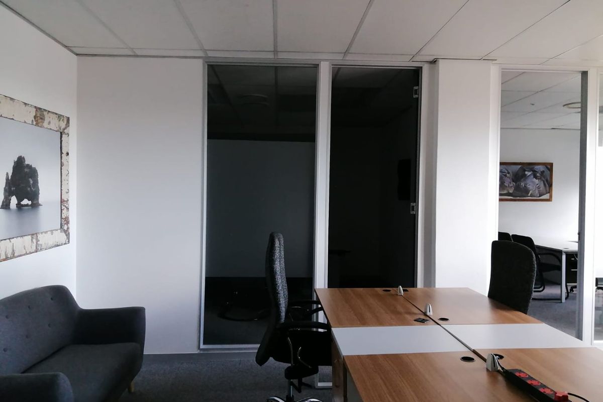 A professional office space featuring glass partition walls, suspended ceiling tiles, and carpeted flooring, suitable for a modern commercial work environment.