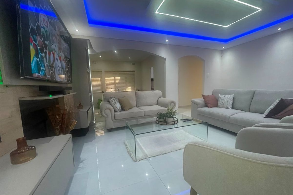 Modern living room featuring polished tiled flooring, recessed ceiling lighting with blue LED accents, and an open-plan archway leading to adjacent living spaces.