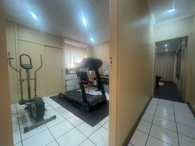 A functional room currently utilized as a home gym, featuring tiled flooring, built-in storage cupboards, and recessed ceiling lighting.