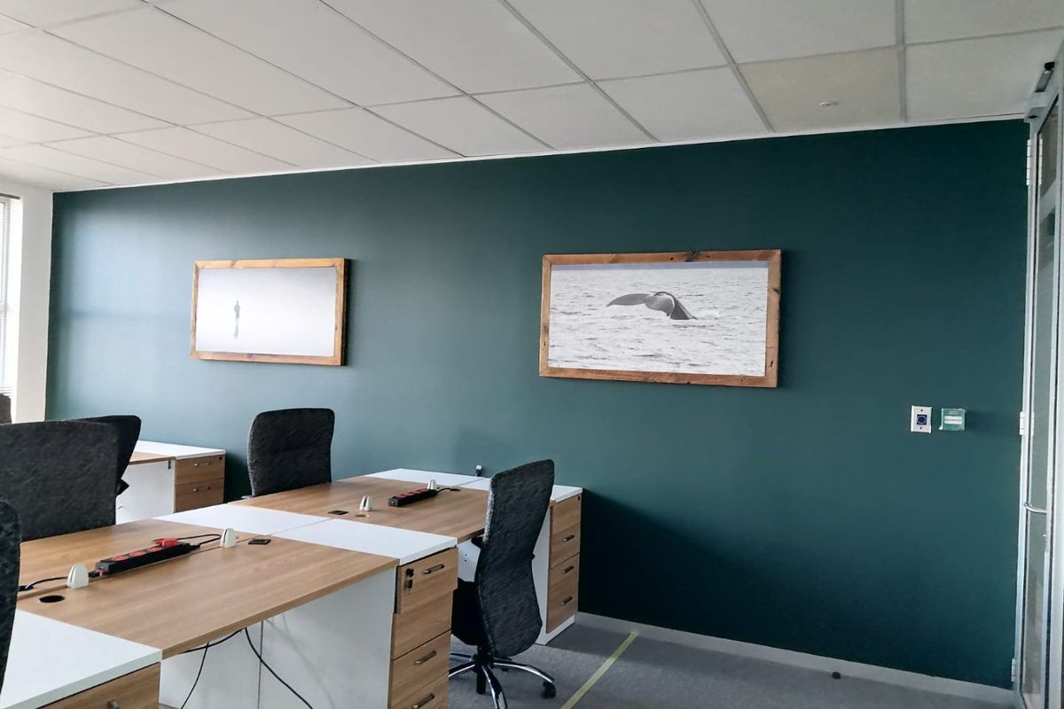 A modern office space featuring a dark green accent wall, suspended ceiling tiles, and carpeted flooring, providing a professional work environment.