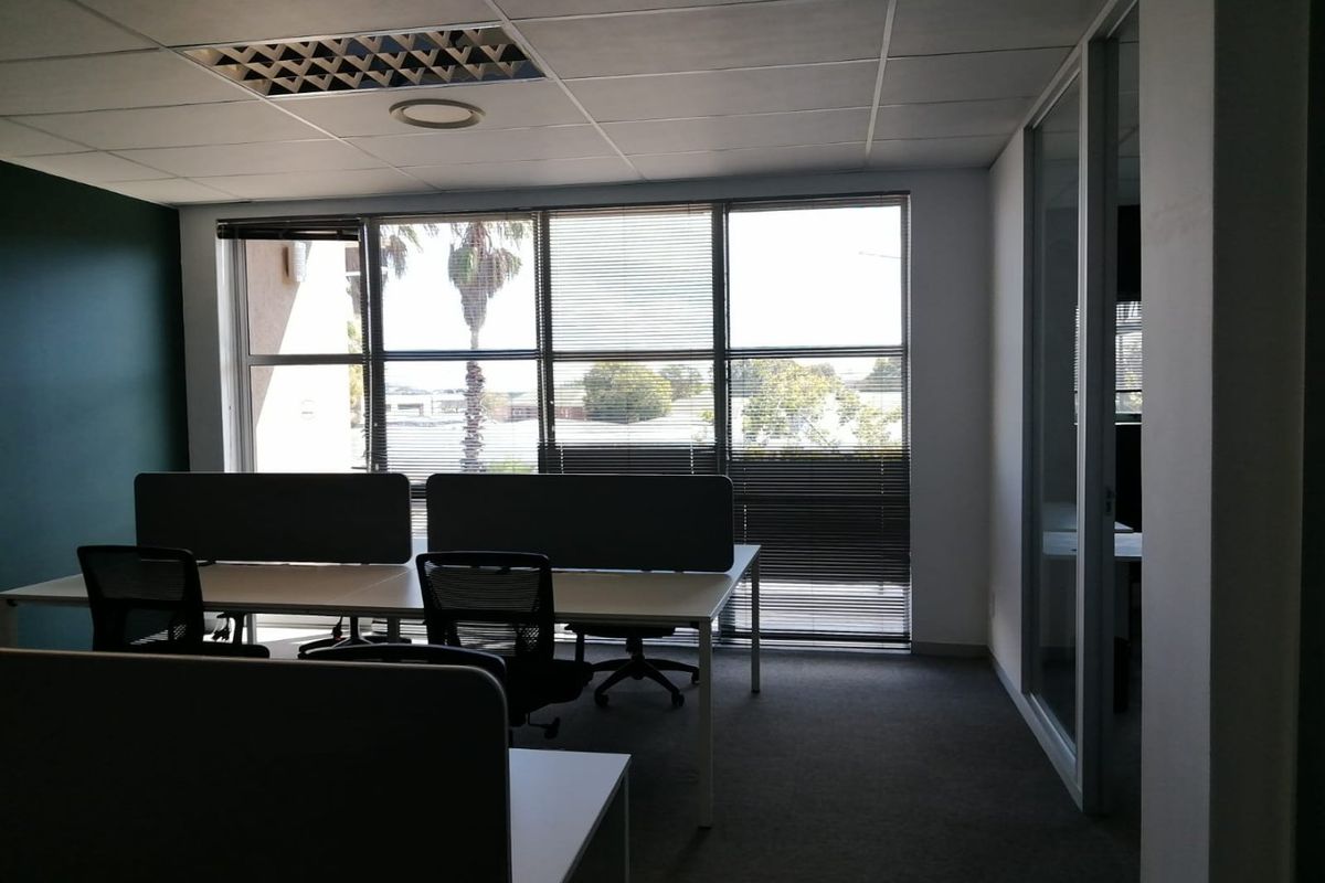 A professional office space featuring a suspended ceiling, large windows with venetian blinds, and a glass partition wall, providing a bright and functional workspace.