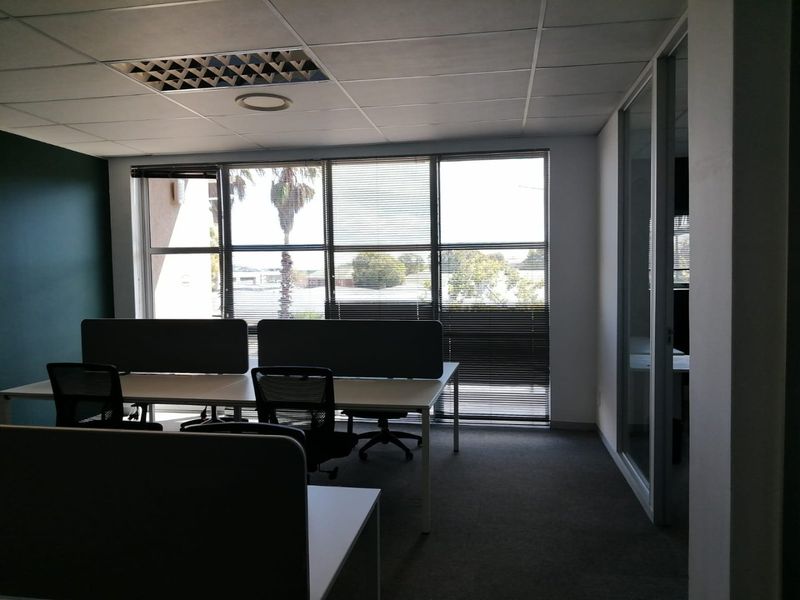 A professional office space featuring a suspended ceiling, large windows with venetian blinds, and a glass partition wall, providing a bright and functional workspace.