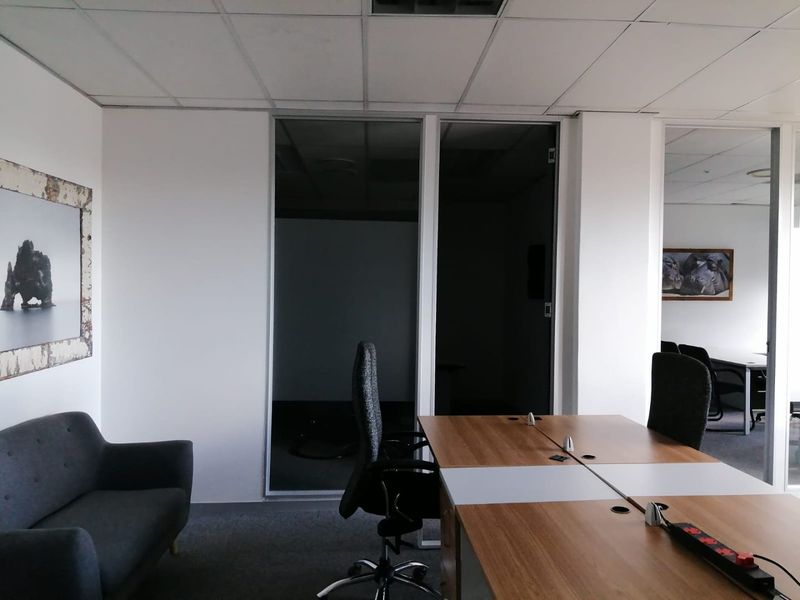 A professional office space featuring glass partition walls, suspended ceiling tiles, and carpeted flooring, suitable for a modern commercial work environment.