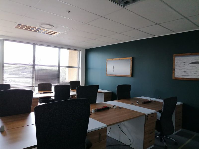 A professional office space featuring a suspended ceiling, recessed lighting, large windows with blinds, and integrated desk workstations.