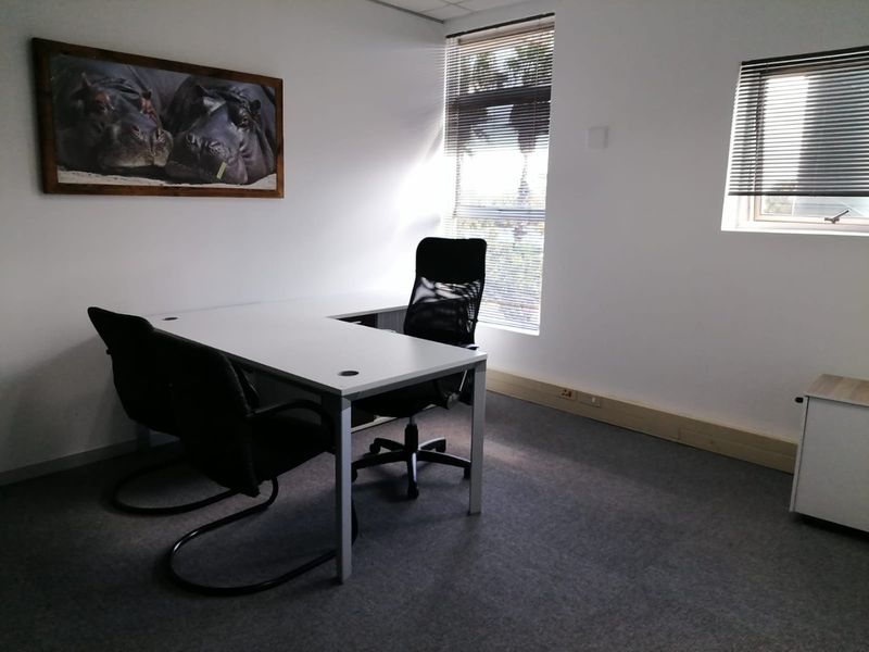 A functional office space featuring carpeted flooring, natural light through venetian blinds, and integrated electrical outlets.