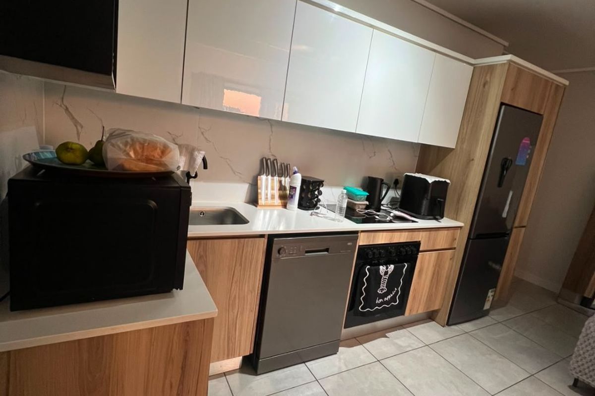 Modern kitchen featuring sleek white upper cabinetry, wood-grain lower cabinets, marble-look splashback, and integrated appliances with contemporary track lighting.