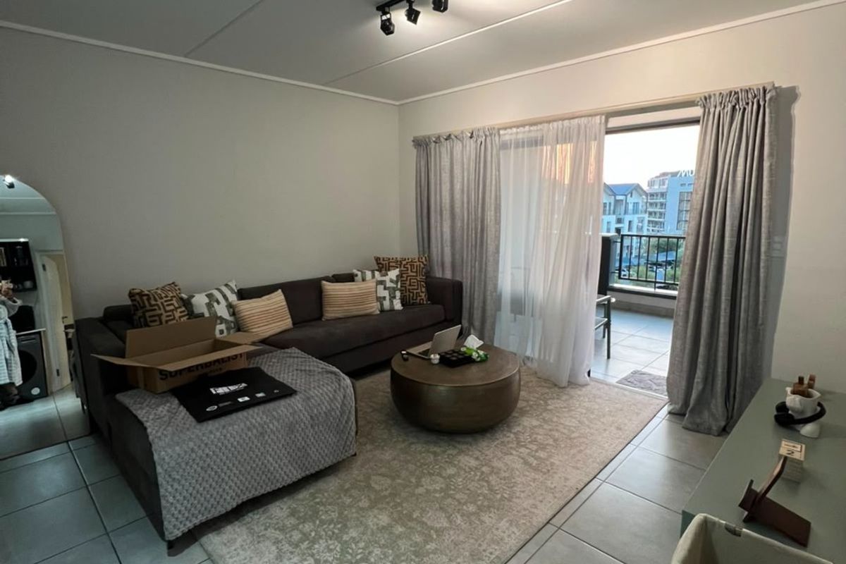 A well-lit living room featuring neutral tiled flooring, modern track lighting, and a large sliding glass door providing access to an outdoor balcony.