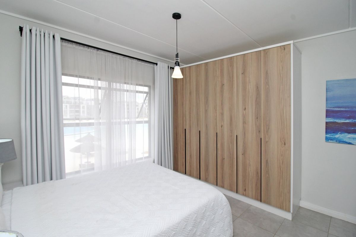 A well-maintained bedroom featuring modern wood-finish built-in wardrobes, neutral tiled flooring, and a contemporary pendant light fixture.