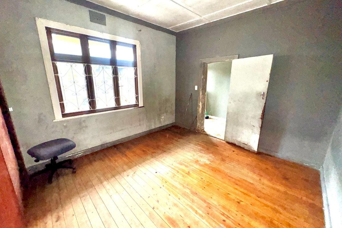 An empty bedroom featuring original timber flooring, security bars on the window, and a ceiling with visible wear, requiring cosmetic updates.