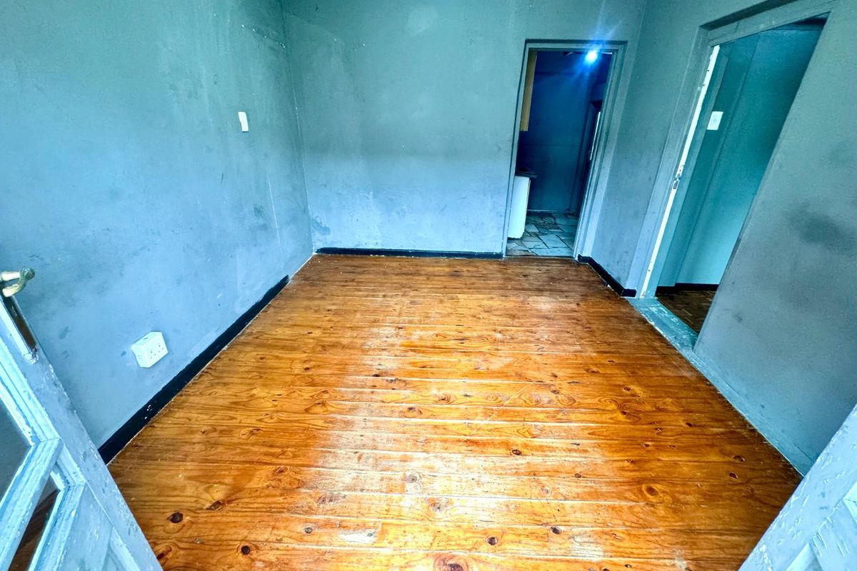 An empty living room featuring polished timber flooring and dark-toned walls, providing a blank canvas for interior design updates.