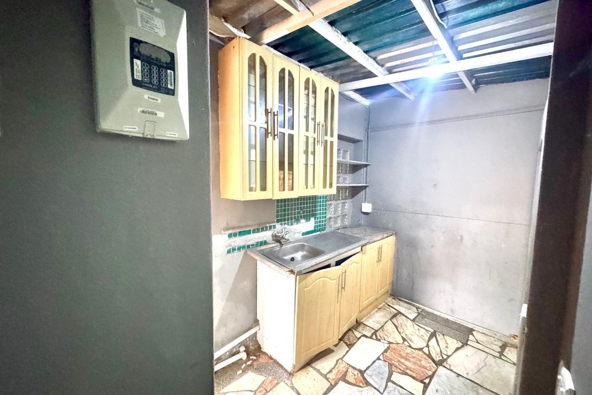 A basic kitchen area featuring built-in cabinetry, a stainless steel sink, and tiled flooring, requiring renovation to improve finishes and overall functionality.