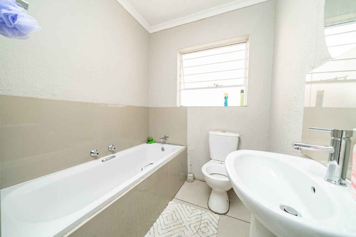 A functional bathroom featuring a bathtub, pedestal basin, and toilet with neutral wall tiling and natural light from a window.