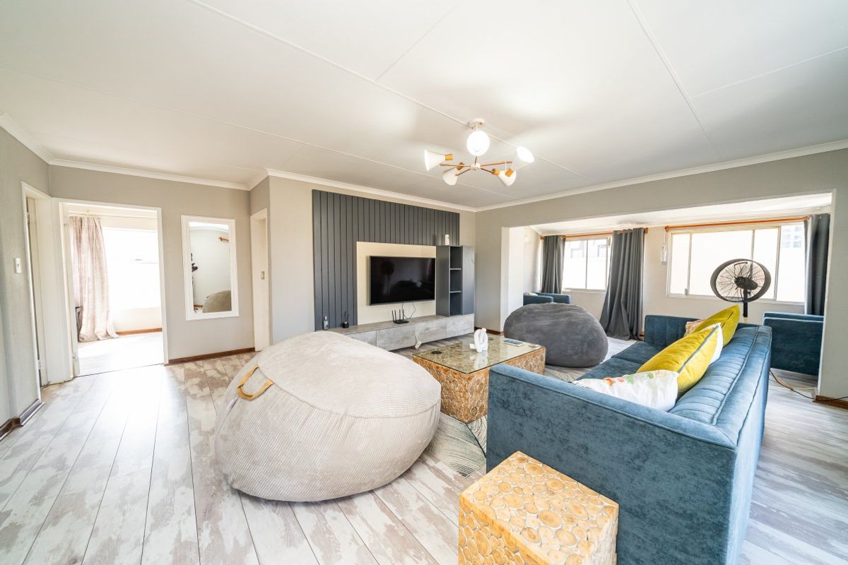 Spacious living room featuring a modern built-in media wall unit, light-toned laminate flooring, and ample natural light from large windows.