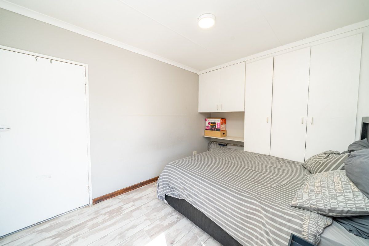 A bedroom featuring built-in white cupboards, light-toned laminate flooring, and neutral wall finishes, offering a functional space with storage.