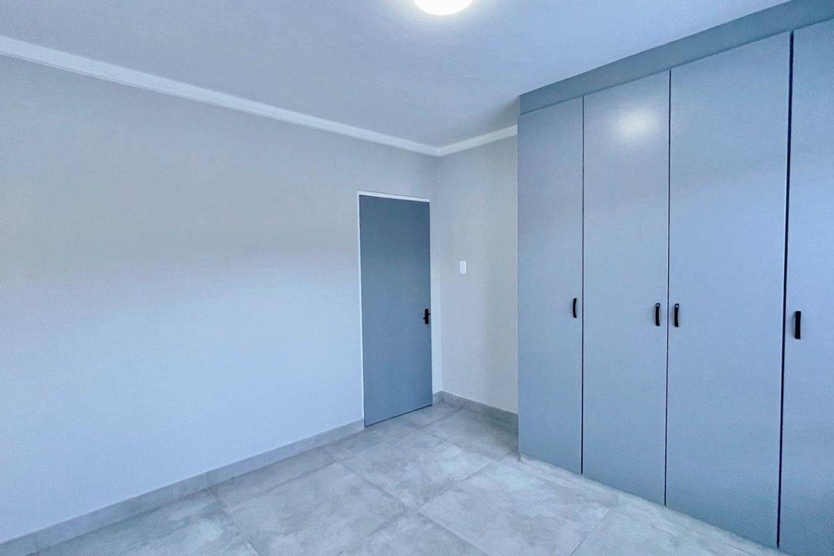 A clean, modern bedroom featuring neutral tiled flooring, built-in cupboards with a contemporary finish, and crisp white walls.