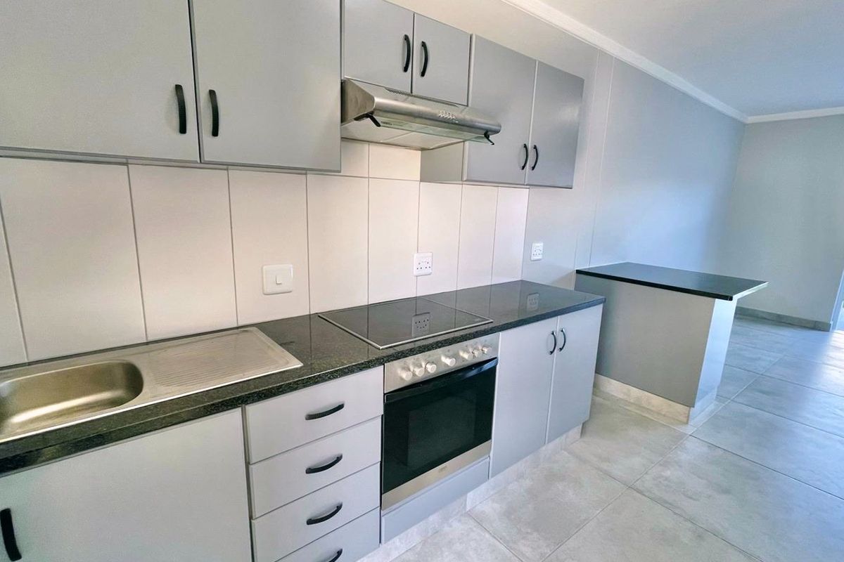 Modern kitchen featuring grey built-in cabinetry, granite countertops, integrated electric hob and oven, and tiled flooring in an open-plan layout.