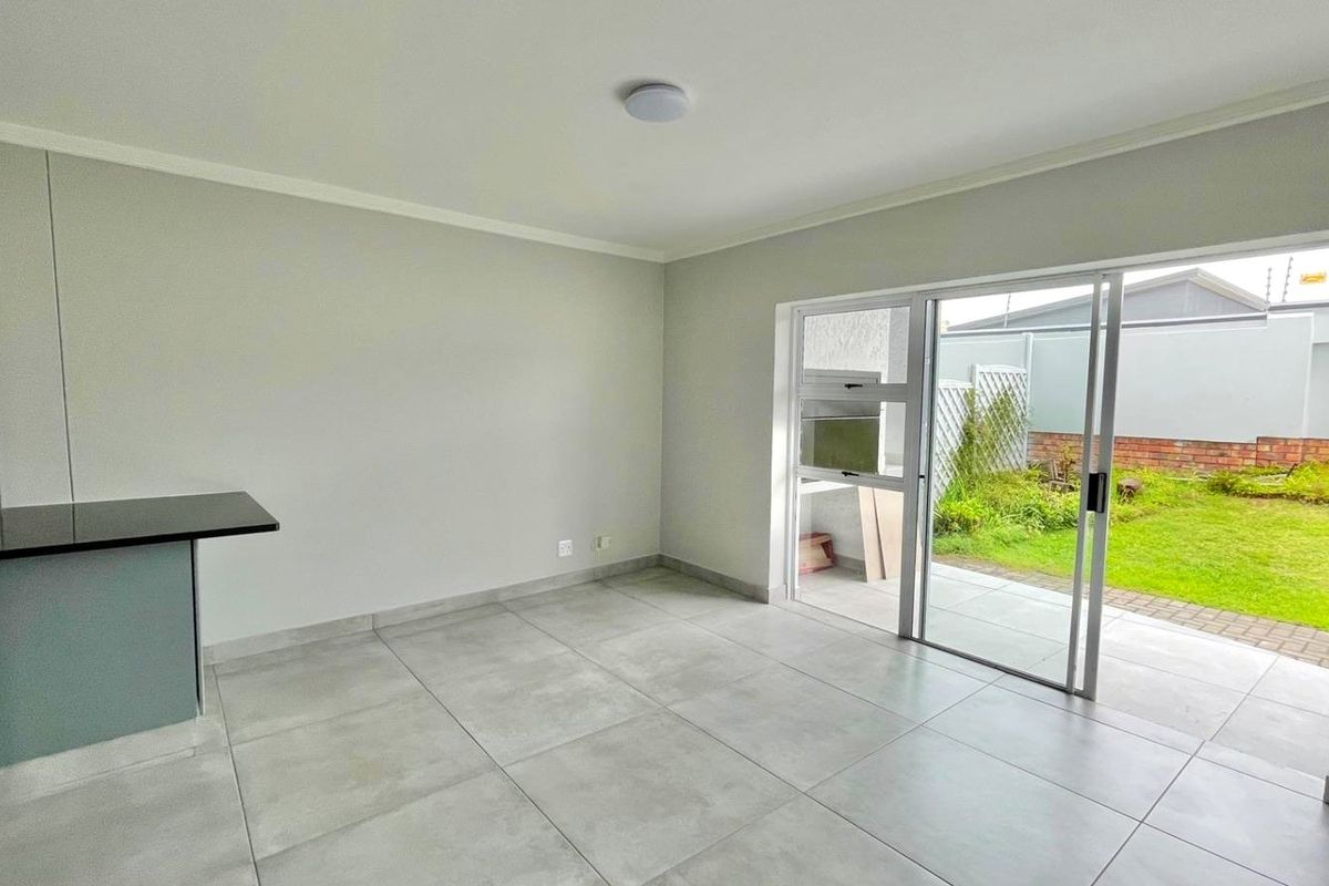 A bright, open-plan living area featuring large format floor tiles, a built-in breakfast bar, and direct access to a private garden through sliding doors.