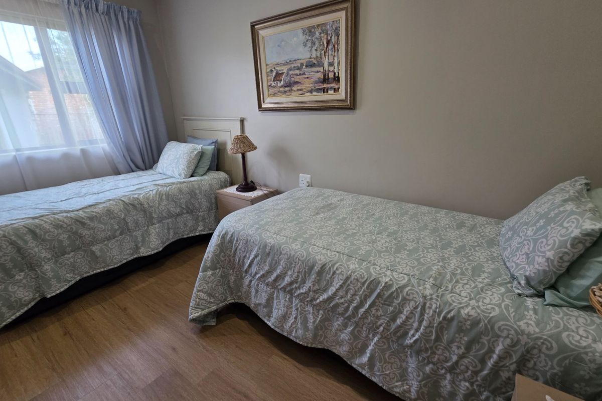 A bedroom featuring laminate flooring and a window with curtains, providing a functional and comfortable living space.