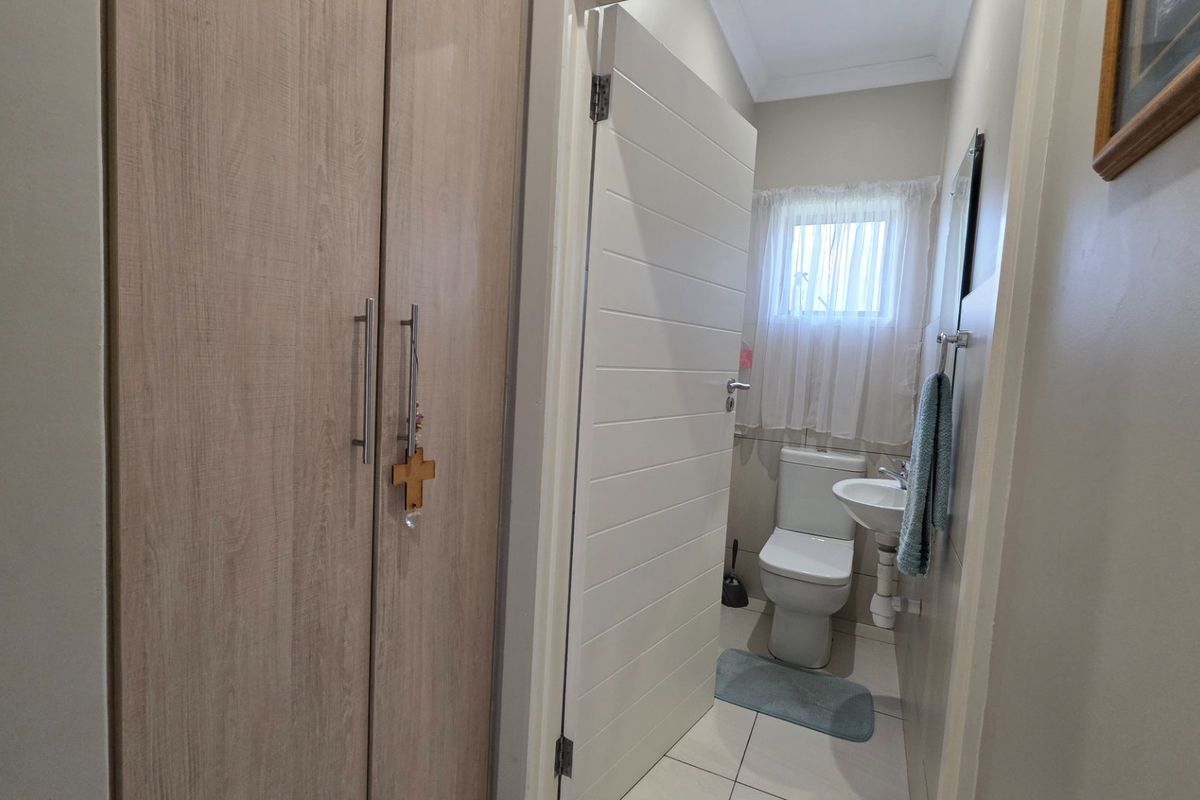 A compact bathroom featuring a pedestal basin, toilet, and tiled flooring, adjacent to a built-in storage cupboard.