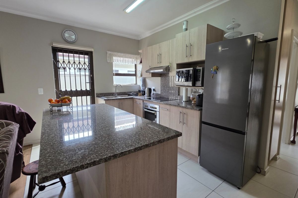 Modern kitchen featuring light wood cabinetry, granite countertops, a central island, and integrated appliances, providing a functional and well-maintained cooking space.